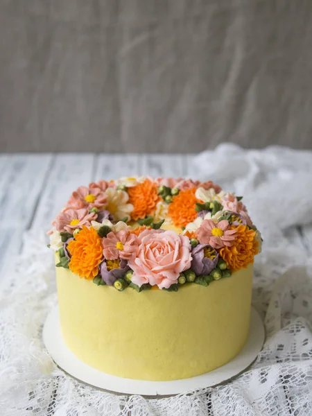 Yellow cream cake decorated with buttercream flowers - peonies, roses, chrysanthemums, scabiosa, carnations - on white wooden background. Cake for birthday. Close up, copy space,