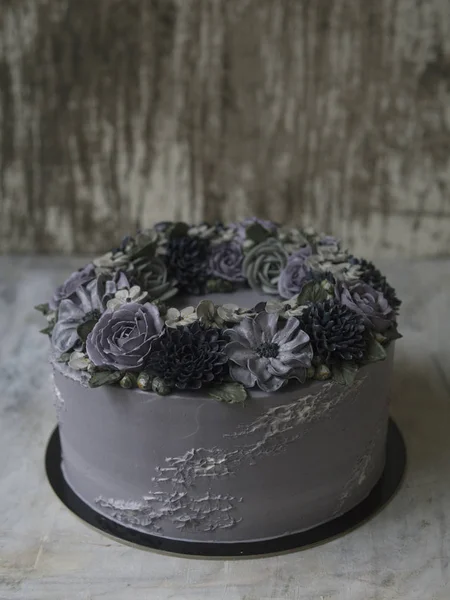 Gray cream cake decorated with dark buttercream flowers on rustic background. Halloween cake. Black cake. Close up, copy space