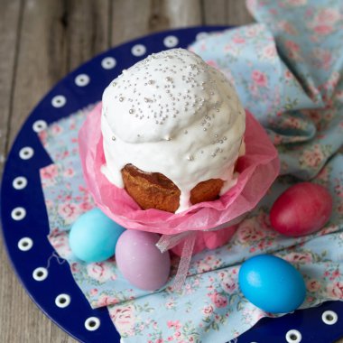 Paskalya kek - kulich. Geleneksel Paskalya tatlı ekmek beyaz buzlanma ve çiçek kumaş ahşap zemin üzerine mavi peçete üzerinde renkli yumurta dekore edilmiştir. Kopya alanı, seçici odak.