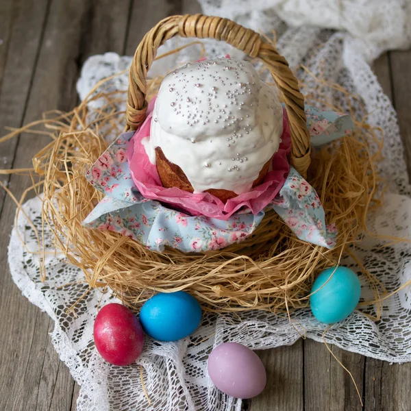 イースター ケーキ クリーチ伝統的なイースターの甘いパンは ストロー バスケット 花柄のファブリックと木製の背景にレース ナプキンに着色された卵の白いアイシングを装飾されています コピー スペース セレクティブ — ストック写真