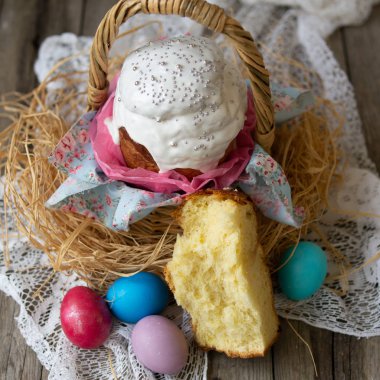 Paskalya pastasından - kulich. Geleneksel Paskalya tatlı ekmek beyaz buzlanma ve çiçek kumaş ahşap zemin üzerine mavi peçete üzerinde renkli yumurta dekore edilmiştir. Kopya alanı, seçici odak.