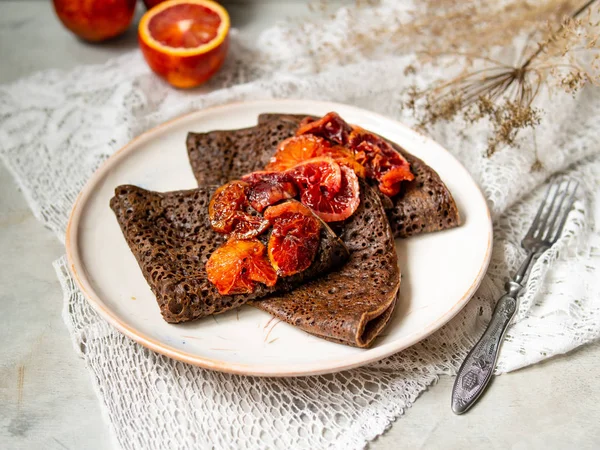 Dantel kumaş ile gri arka plan üzerinde beyaz bir plaka üzerinde kan portakal soslu çikolatalı krep ince. Krep, yığını Rus blin, Maslenitsa. Lezzetli kahvaltı. Yakın, seçici odak