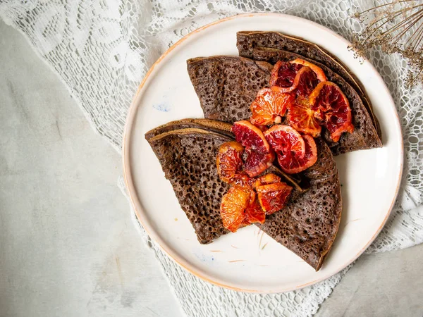 Dantel kumaş ile gri arka plan üzerinde beyaz bir plaka üzerinde kan portakal soslu çikolatalı krep ince. Krep, yığını Rus blin, Maslenitsa. Lezzetli kahvaltı. Yakın, seçici odak