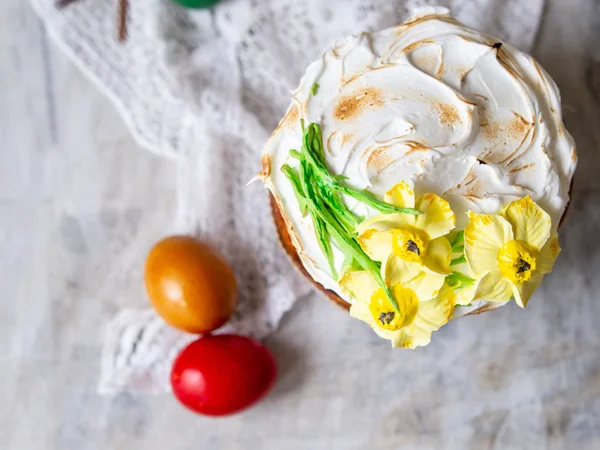 Paskalya pastası Kulich. Geleneksel Paskalya tatlı ekmek süslenmiş Meringue, dantel kumaş ve renkli yumurta ile ahşap gri arka plan üzerinde sarı nergis. Kopyala boşluk, üst görünüm. mevsim tebrik kartı.