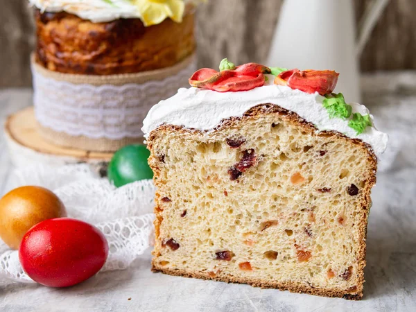 Easter cake kulich. Traditional sweet bread decorated meringue, yellow daffodils on gray background with lace fabric and colored eggs. Copy space, selective focus.Slice of cake.seasons greetings card