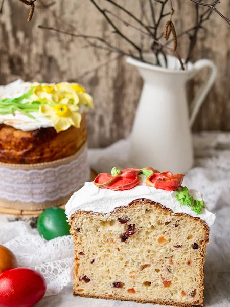 Easter cake kulich. Traditional sweet bread decorated meringue, yellow daffodils on gray background with lace fabric and colored eggs. Copy space, selective focus.Slice of cake.seasons greetings card