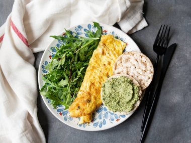 Sağlıklı kahvaltı-omlet, roka ve gri arka planda pesto ile ekmek. Taze roka ve pesto kraker ile mükemmel yumurta omlet. Vejeteryan yemekleri. Diyet. Seçici odaklama, yakın çekim.