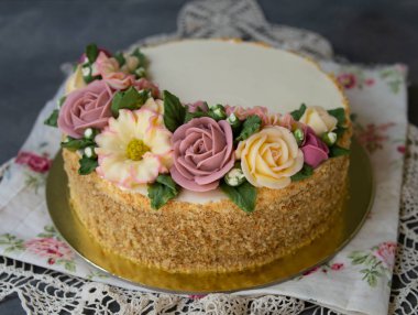 Beyaz kremalı ballı pasta, tereyağlı çiçeklerle süslenmiş şakayıklar, güller, kasımpatılar, gri arka planda dantel kumaşlı scabiosa. Yaklaş, seçici odaklanma