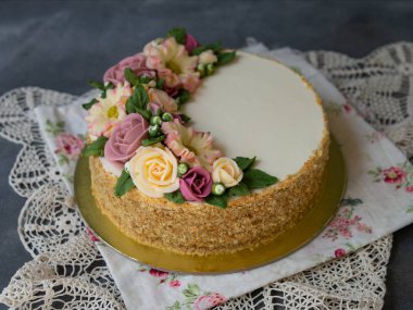 Beyaz kremalı ballı pasta, tereyağlı çiçeklerle süslenmiş şakayıklar, güller, kasımpatılar, gri arka planda dantel kumaşlı scabiosa. Yaklaş, seçici odaklanma