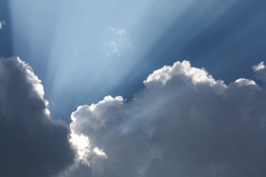 Bulutlardan çıkan güneş ışınlarıyla güzel mavi gökyüzü, cennet. Beyaz kıvırcık bulutlar, ilahi ışık. Işınlar.