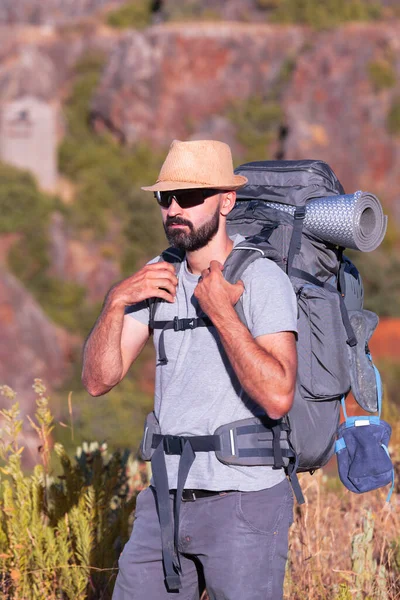 Hispanic male trekker with sunglasses holding on to a full backpack — Stock Photo, Image