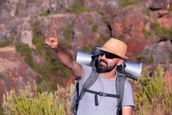 Güneş gözlüklü İspanyol erkek yürüyüşçü gülümsüyor ve çerçeveden dışarı işaret ediyor.