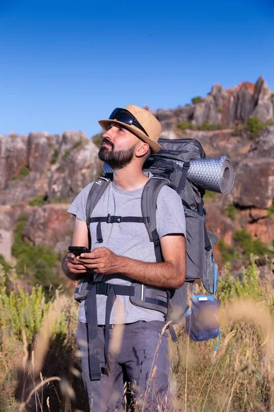 Confused hispanic male trekker holding his smartphone and looking up — Stock Photo, Image
