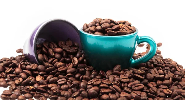 Kahve çekirdekleri ile dolu iki güzel kahve fincanını kapat ve etrafa saçılan bir yığın fasulye ile birlikte. Beyazda izole edilmiş.
