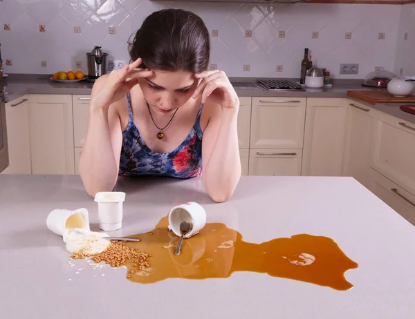 Pretty young woman upset looking at a mess on the kitchen counter