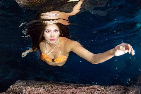 black hair Mermaid swimming underwater in the deep blue sea and looking at you