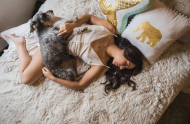 Kız uzanıyor, dinleniyor ve kestiriyor, beyaz bir battaniye giyip, Schnauzer köpeğinin yanında yatıyor, bir öğleden sonra rahatlıyor ve evcil hayvanının yanında..