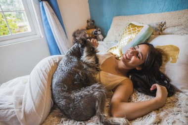 Beyaz bir battaniye elbisesi içinde yatağında Schnauzer köpeğinin yanında uzanmış, dinleniyor ve oyun oynuyor. 3