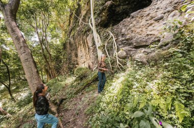 Anne ve kız kamp kıyafetleri içinde ormanda bir mağaraya doğru yürüyorlar..