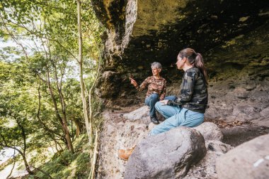 Anne ve kız kamp kıyafetleri giyip ormanın ortasında eski bir mağaranın girişinde dinleniyorlar..