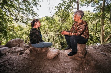 Anne ve kız kamp kıyafetleri giyip ormanın ortasında eski bir mağaranın girişinde dinleniyorlar..