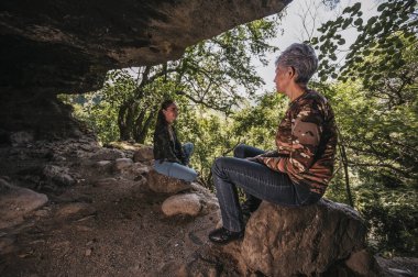 Anne ve kız kamp kıyafetleri giyip ormanın ortasında eski bir mağaranın girişinde dinleniyorlar..