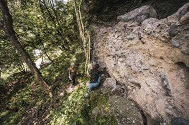 Anne ve kız kamp kıyafetleri içinde ormanda bir mağaraya doğru yürüyorlar..