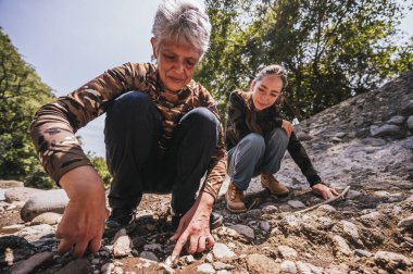 Anne ve kız bitkiler, taşlar, böcekler gibi küçük detayları gözlemler ve nehir kenarında iyi vakit geçirirler..