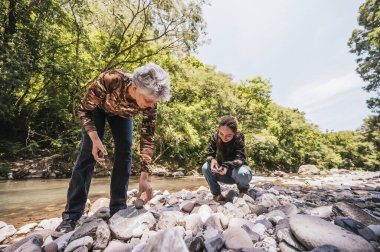 Anne ve kız bitkiler, taşlar, böcekler gibi küçük detayları gözlemler ve nehir kenarında iyi vakit geçirirler..