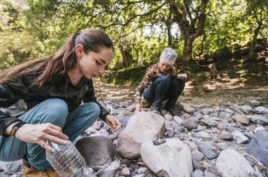 Anne ve kızı nehrin kenarında apacheta yaparken eğleniyorlar, gülümsüyorlar ve anın tadını çıkarıyorlar..