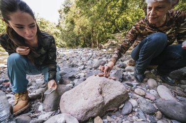 Anne ve kızı nehrin kenarında apacheta yaparken eğleniyorlar, gülümsüyorlar ve anın tadını çıkarıyorlar..