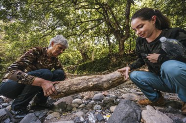 Anne ve kızı nehrin kenarında apacheta yaparken eğleniyorlar, gülümsüyorlar ve anın tadını çıkarıyorlar..