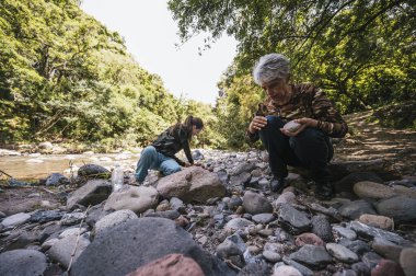 Anne ve kızı nehrin kenarında apacheta yaparken eğleniyorlar, gülümsüyorlar ve anın tadını çıkarıyorlar..