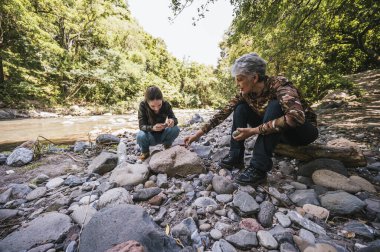 Anne ve kızı nehrin kenarında apacheta yaparken eğleniyorlar, gülümsüyorlar ve anın tadını çıkarıyorlar..