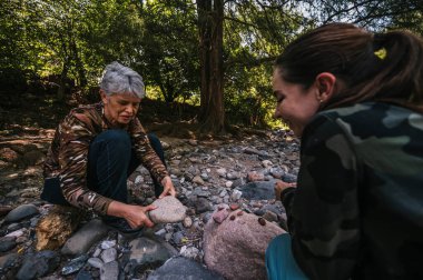 Anne ve kızı nehrin kenarında apacheta yaparken eğleniyorlar, gülümsüyorlar ve anın tadını çıkarıyorlar..