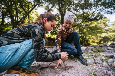 Anne ve kızı nehrin kenarında apacheta yaparken eğleniyorlar, gülümsüyorlar ve anın tadını çıkarıyorlar..
