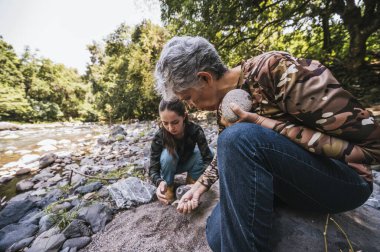 Anne ve kızı nehrin kenarında apacheta yaparken eğleniyorlar, gülümsüyorlar ve anın tadını çıkarıyorlar..