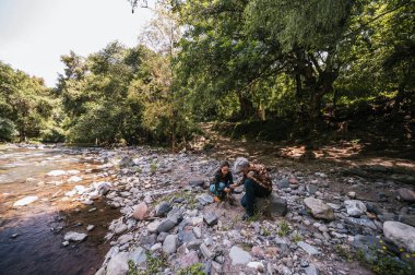 Anne ve kızı nehrin kenarında apacheta yaparken eğleniyorlar, gülümsüyorlar ve anın tadını çıkarıyorlar..