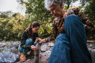 Anne ve kızı plastik bir şişede nehir kumu topluyor, gülümsüyor ve anın tadını çıkarıyorlar..
