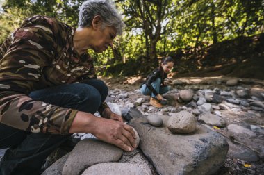 Anne ve kızı nehrin kenarında apacheta yaparken eğleniyorlar, gülümsüyorlar ve anın tadını çıkarıyorlar..