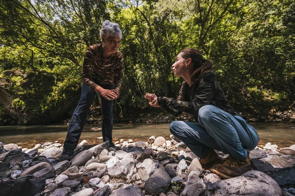 Anne ve kız bitkiler, taşlar, böcekler gibi küçük detayları gözlemler ve nehir kenarında iyi vakit geçirirler..