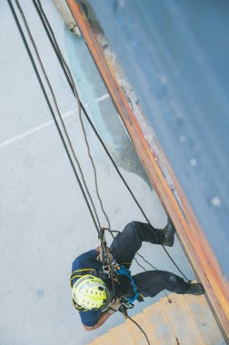 Firefighter rescuer descending a massive wall using a rappelling device in a multi-story building, wearing protective gear such as a helmet, harness, and carabiners.