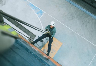 Firefighter rescuer descending a massive wall using a rappelling device in a multi-story building, wearing protective gear such as a helmet, harness, and carabiners.