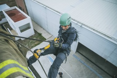 Female firefighter rescuer beginning the descent of a huge wall using the rappelling device in a multi-story building.