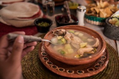 POV photo of Rat broth, a typical dish from the state of Zacatecas, Mexico, accompanied by chopped vegetables and a whole field rat, served in a clay dish.