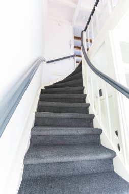 Gri halılı sert merdivenler ve yukarıdan görünen beyaz duvarlar.