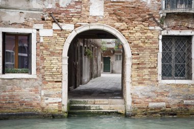 İtalya 'da Venedik' te bir kanalın yanındaki turuncu tuğla binanın küçük arka kapısı.