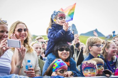 Traena, Norveç - 7 Temmuz 2017: Norveçli eşcinsel korosu Oslo Fagittkor'un Traenafestival'deki konseri sırasında annesinin omzunda küçük kız izliyor ve tezahürat yapıyor, traena adasında müzik festivali gerçekleşiyor