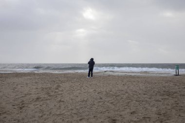 Fırtınadan önce sahilde rüzgara karşı resim çekmeye çalışan adam Carmen, La Faute Sur Mer, Vendee, Fransa kıyılarını vurmadan önce