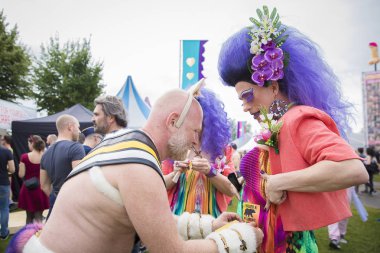 Amsterdam, Hollanda - 29 Temmuz 2017: Ayı kılığına girmiş bir adam bir ayıya sarıldığımı söyleyen bir etiket yapıştırıyor ve Westerpark'taki Milkshake Festivali'nde bir travestide beğendim.